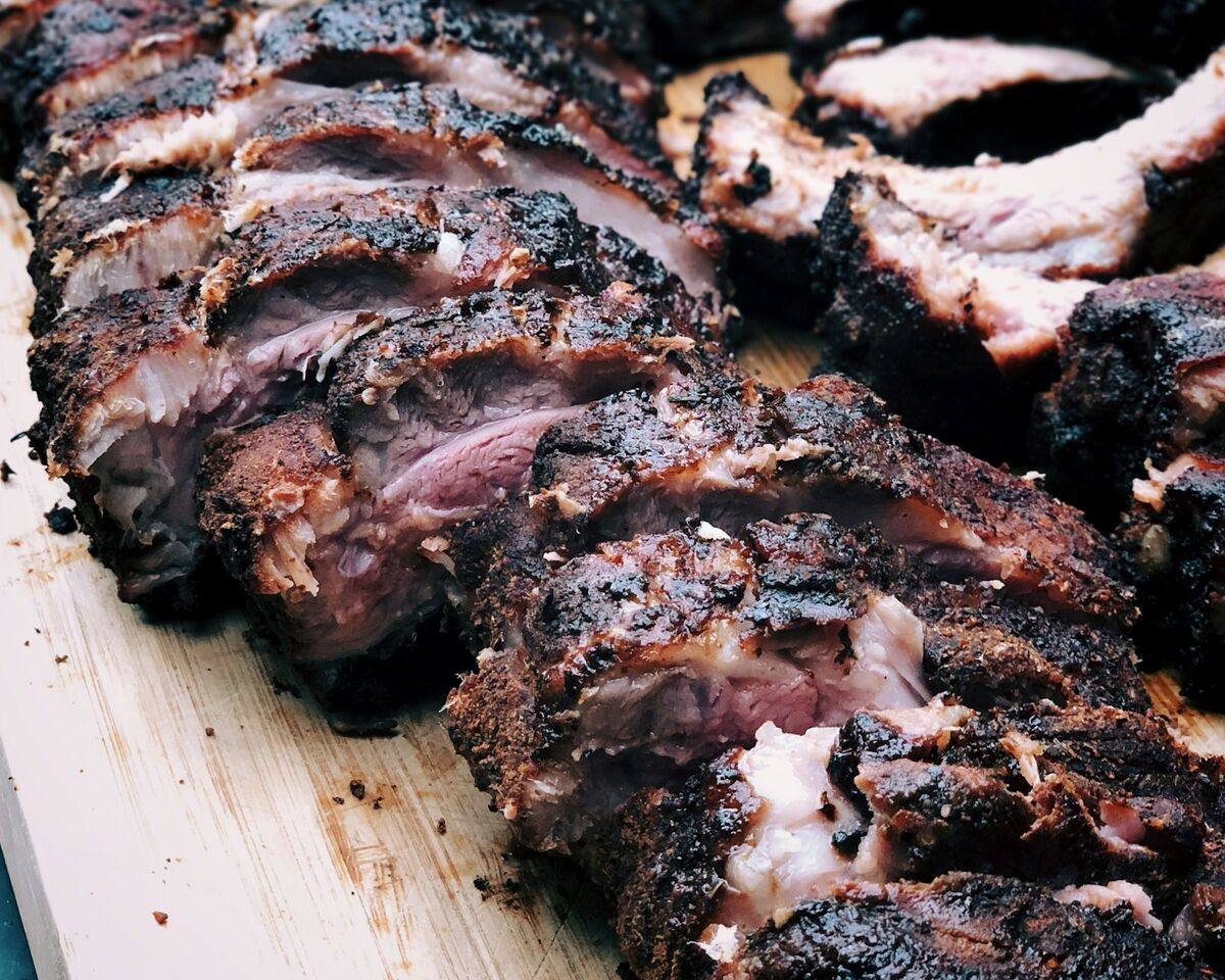 Plate-cut beef ribs resting on a board after a long cook, bark almost black.