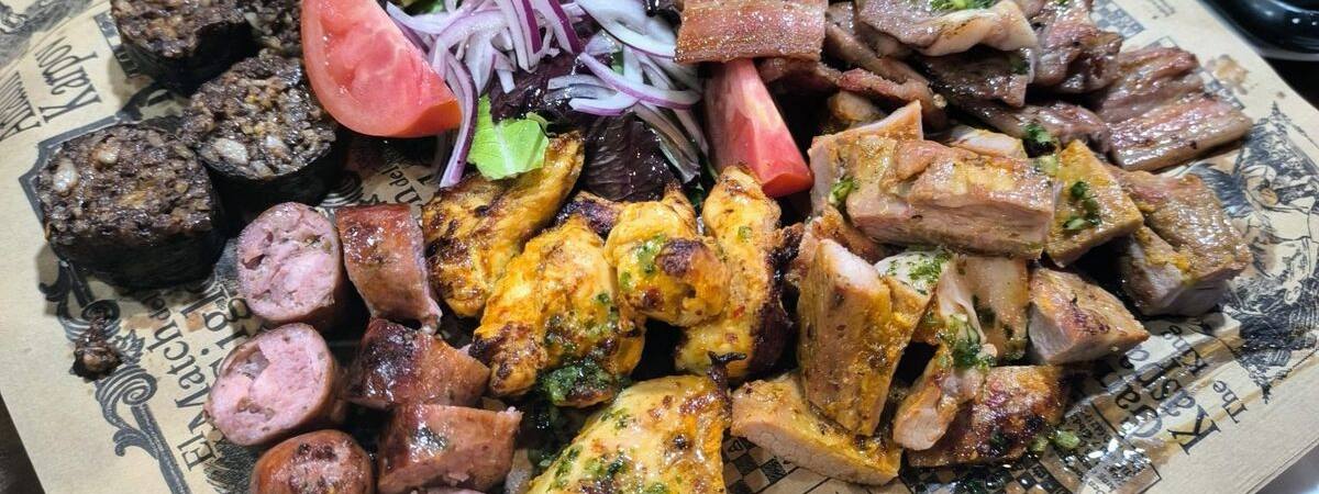 A large mixed grill spread out on paper for the table to share, with pickled onion and lemon.